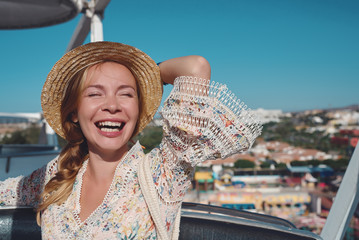 The portrait of a young beautiful European woman. She is sitting in a Ferris wheel, having fun, enjoying her holidays and smiling to the camera.