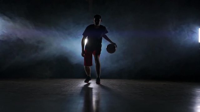 one young adult man, basketball player dribble ball, dark indoors basketball court slow motion
