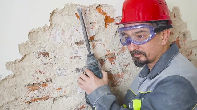 portrait of an adult man in a helmet on his head and with a perforator in his hand