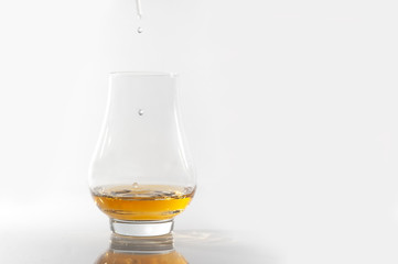 Three drops of water being added to a glass of whisky, neutral white surface