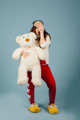 A beautiful young woman wearing pajamas hugging her stuffed teddy bear