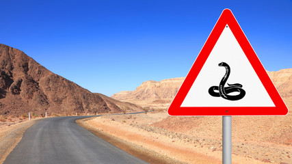Warning road sign - Animals on the road (snake). Stony desert and mountains landscape