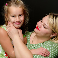 Mom and daughter are hugging on a black background.