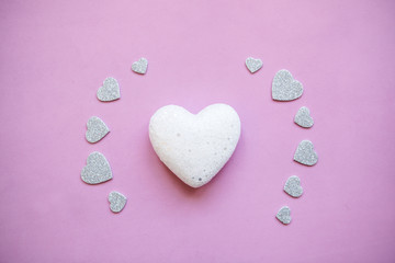 Fototapeta premium White heart on a pink background and near a lot of little hearts. Concept for Valentine's Day or Women's Day or the topic of health, life and help or care for children. Big heart symbol of kindness.