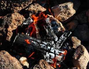 Obraz premium Hot bright bonfire at stones on sunny day. Burning logs. Glow flame