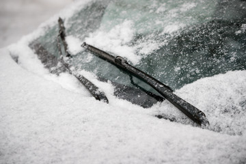 Car wiper blades clean snow from car windows. Flakes of snow covered the car with a thick layer. Safe driving with working wipers and clean windshield. - obrazy, fototapety, plakaty