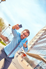 Funny businessman with thumbs up while using smartphone outdoors.