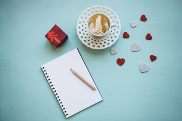Fresh cappuccino coffee on a blue background. Near empty diary to write and a box with a gift. Concept for Valentine's Day or Women's Day.