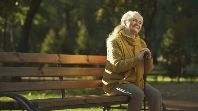 Happy aged woman enjoying warm sunny day sitting on bench in park, retirement