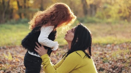 Happy young mother and her little redhead daughter having Fun in an autumn park. They playing, kissing, hugging and laughing. Slow motion