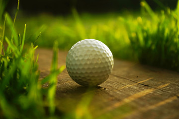 Blurred golf ball on wooden floor in beautiful golf course at sunset background.