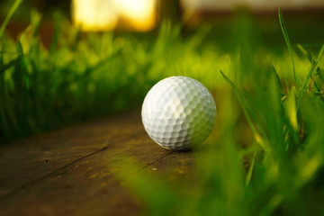 Blurred golf ball on wooden floor in beautiful golf course at sunset background.