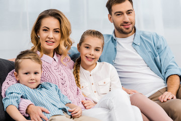 happy family sitting on sofa and looking at camera in apartment