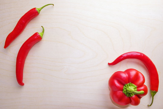 Red fresh hot chili peppers and sweet bell peppers on wooden background with space for lettering