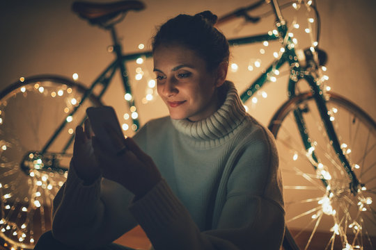 Smiling girl using smartphone with christmas lights on the bicycle in the background