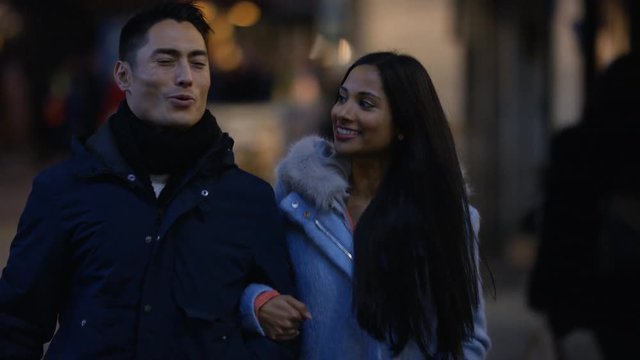 Young diverse mixed couple walking arm in arm in the street at night
