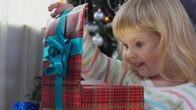 Girl sitting under Christmas tree and opening boxes with presents