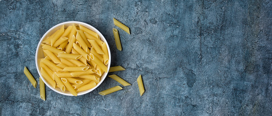 Italian raw penne rigate pasta on blue concrete background