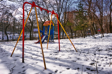 empty bright playground with broken parts and without a swing on the street in winter on a frosty day with snow