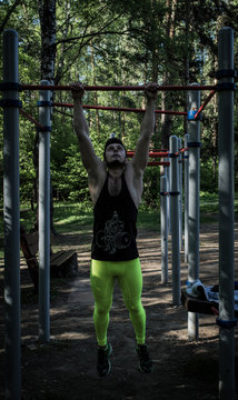 Athletic man pulls himself up on the horizontal bars in the park