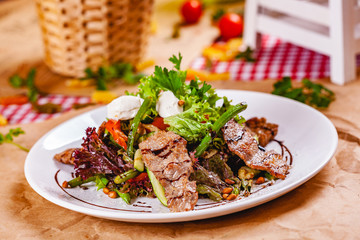Salad with fried meat, pine nuts, vegetables and mozzarella cheese on white plate. Close up