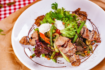 Salad with fried meat, pine nuts, vegetables and mozzarella cheese on white plate. Close up