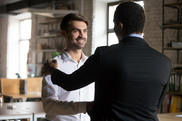 Happy caucasian employee getting rewarded promoted hired feeling proud shaking hand of black...
