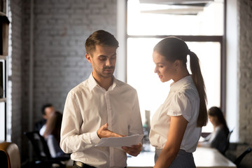 Team leader mentor teaching young employee discussing paperwork standing in office, corporate employees talking about document, executive manager giving instructions explain work to colleague intern