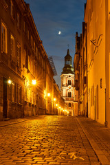 A cobbled street with a baroque belfry of a historic monastery at night in Poznań.