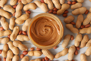  creamy peanut butter in a glass jar and peanuts beans on wooden background top view