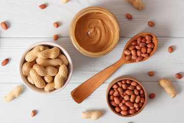  creamy peanut butter in a glass jar and peanuts beans on wooden background top view