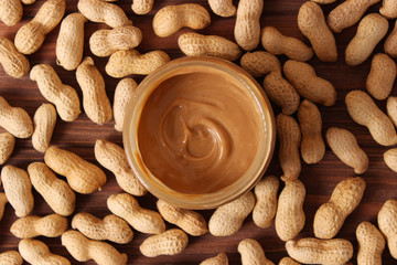  creamy peanut butter in a glass jar and peanuts beans on wooden background top view