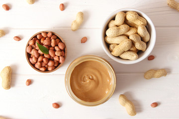  creamy peanut butter in a glass jar and peanuts beans on wooden background top view