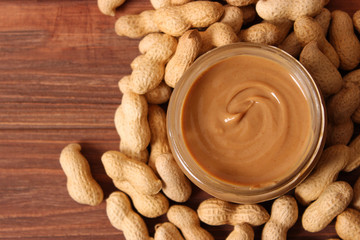  creamy peanut butter in a glass jar and peanuts beans on wooden background top view