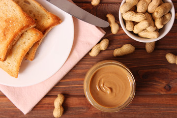  creamy peanut butter in a glass jar and peanuts beans on wooden background top view