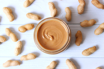  creamy peanut butter in a glass jar and peanuts beans on wooden background top view