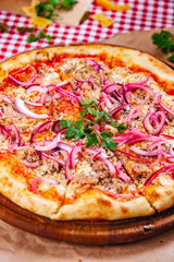 Pizza with tuna and red onion on wooden cutting board. Close up