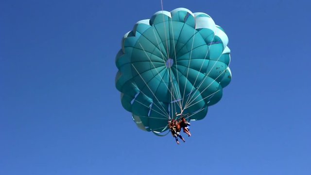 Parasailing by parachute behind boat over waters of blue sea near beach. People tourist flying on parachute over lake in sunny weather. Vacation parasailing activity