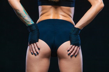 Black boxing bandages on the hands of a muscular girl in black clothes lie on the elastic buttocks. Close-up. Boxing, kickboxing, karate. Fitness, healthy lifestyle concept. Isolated on the black