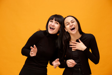 A portrait of a happy smiling mother and daughter at studio on gold background. Trendy colors. Human positive emotions and facial expressions concept