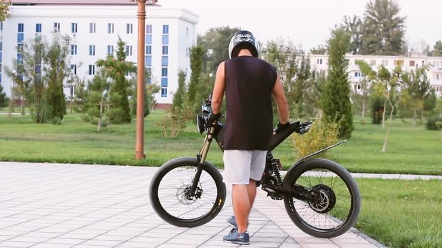Young man biker wearing helmet and sitting on electric bike turning ignition key and riding. Ebike bicycle environmentally friendly eco e-mountainbike transport. Healthy lifestyle