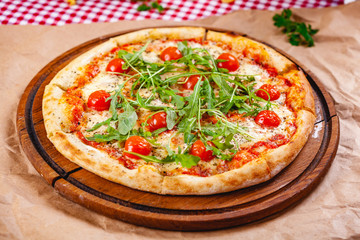 Italian Pizza with tomatoes, mozzarella cheese and arugula on wooden cutting board. Close up