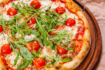 Italian Pizza with tomatoes, mozzarella cheese and arugula on wooden cutting board. Close up