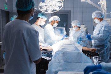 Serious skillful male surgeon standing in the operation theater and taking an instrument while the...