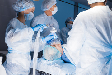 Anesthetists in uniform and masks working together in a surgical room, Team of surgeon prepare to...