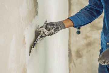 master is applying white putty on a wall and smearing by putty knife in a room of renovating house...