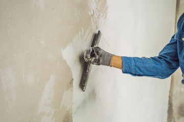 master is applying white putty on a wall and smearing by putty knife in a room of renovating house...