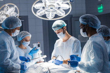 Urgent surgery. Professional smart intelligent surgeons standing near the patient and performing an operation while saving his life. Professional treatment and professional conduct concept.