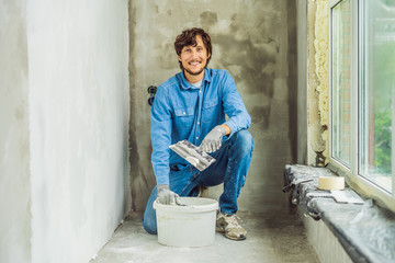 master is applying white putty on a wall and smearing by putty knife in a room of renovating house...