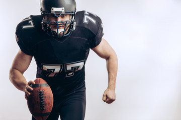 American football player wearing black helmet and jersey serving the ball in motion isolated over...